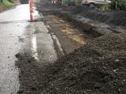 22nd Ave with piles of ground asphalt.  The existing asphalt is recycled to use as base aggregate under the new sidewalk. 