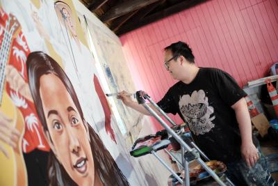 Artist Alex Chiu painting a mural panel